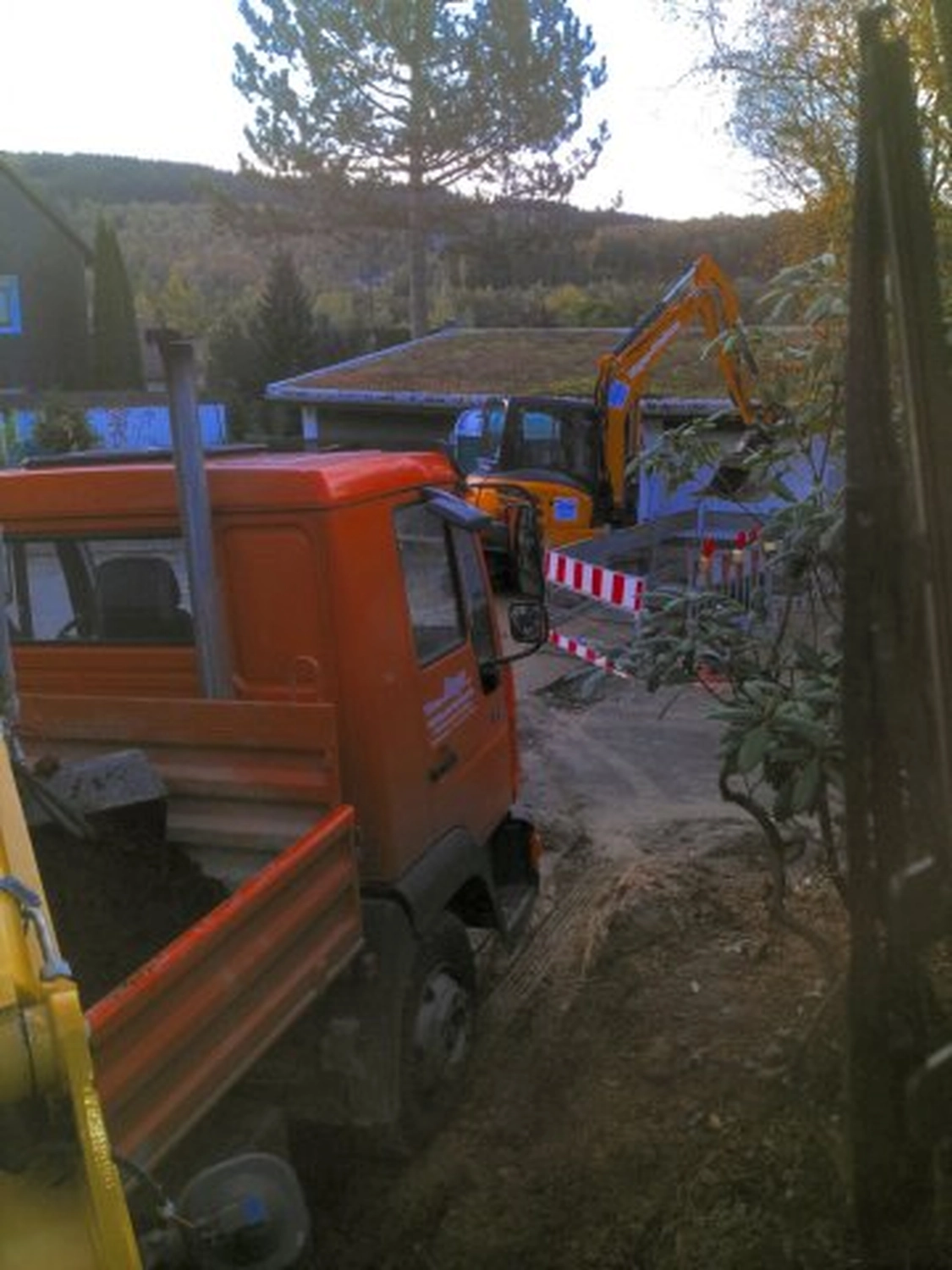 Hans Werner Meyer GmbH - Tiefbauunternehmen - Ein orangefarbener Muldenkipper und ein gelber Bagger auf einer Baustelle in einem hügeligen, bewaldeten Gebiet.