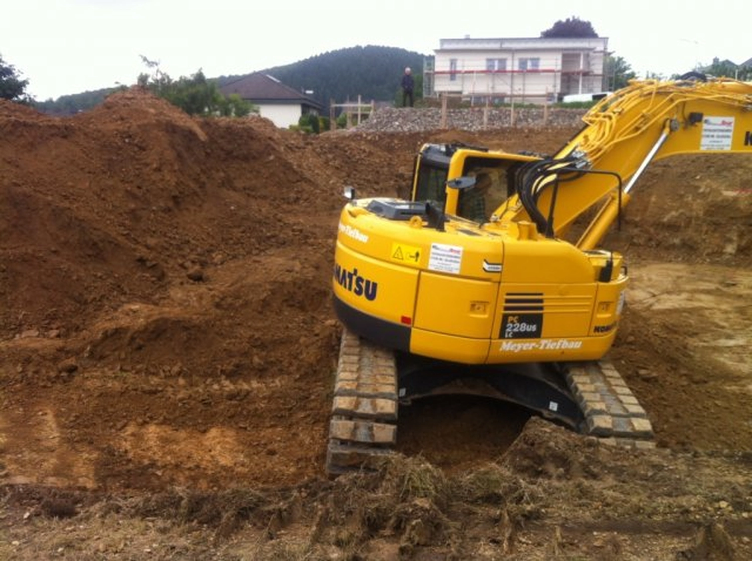 Hans Werner Meyer GmbH - Tiefbauunternehmen - Ein gelber Komatsu PC228US Hydraulikbagger steht auf einer großen Erdbaustelle neben einem Haufen brauner Erde.