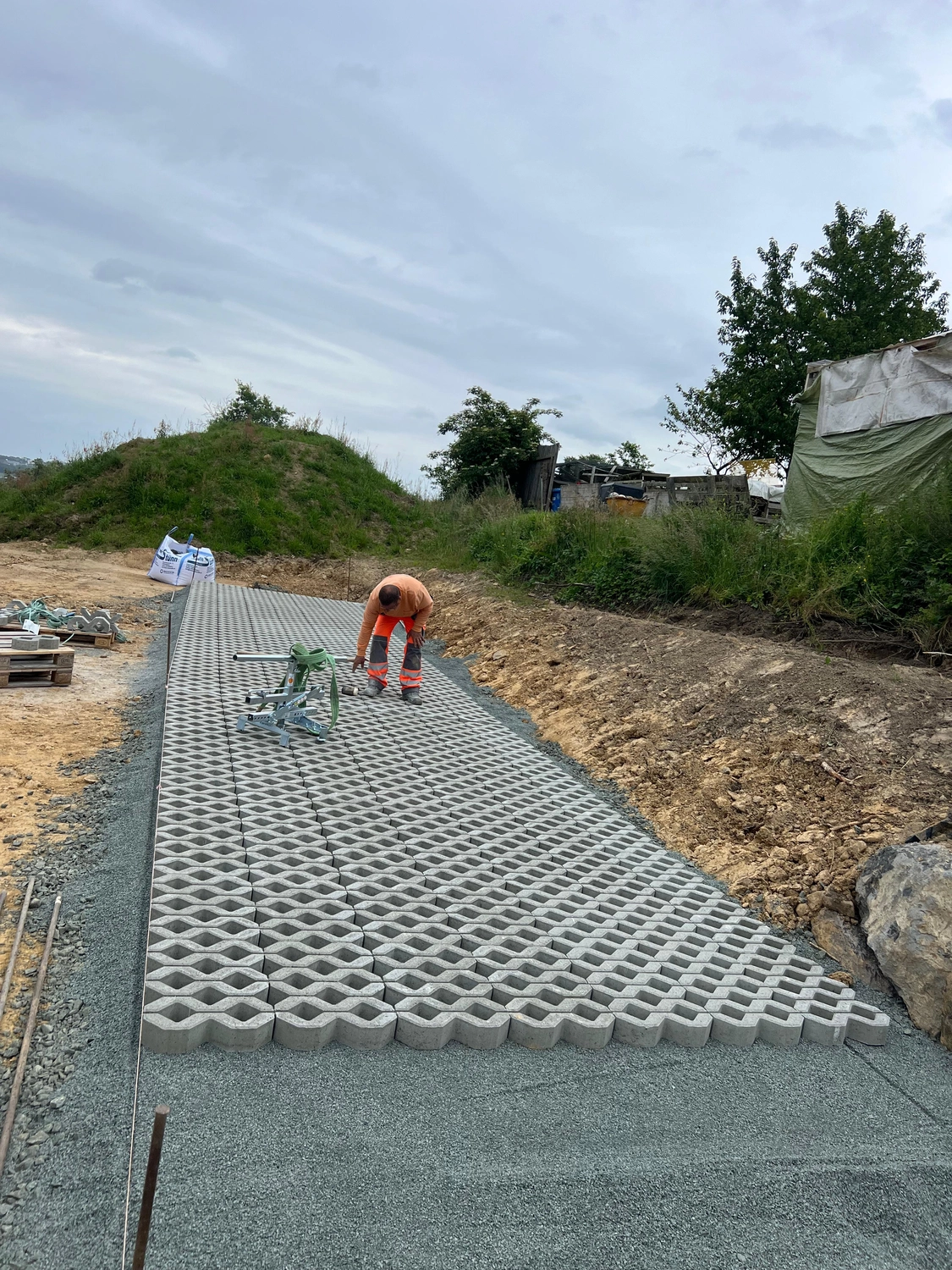 Hans Werner Meyer GmbH - Tiefbauunternehmen - Ein Bauarbeiter verlegt wasserdurchlässige Betonrasenpflastersteine ​​für eine Einfahrt auf einem Kiesbett.